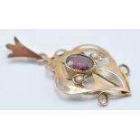 A late 19th Century Victorian Art Nouveau 9ct gold pendant being set with an oval cut garnet flanked