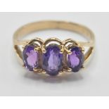 A 9ct gold three stone ring being set with three oval cut purple stones with pierced shoulders. Band
