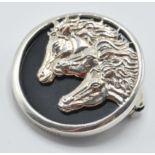 A sterling silver and onyx brooch set with three horse heads. Measures: 3cm diameter. weight 12.8g