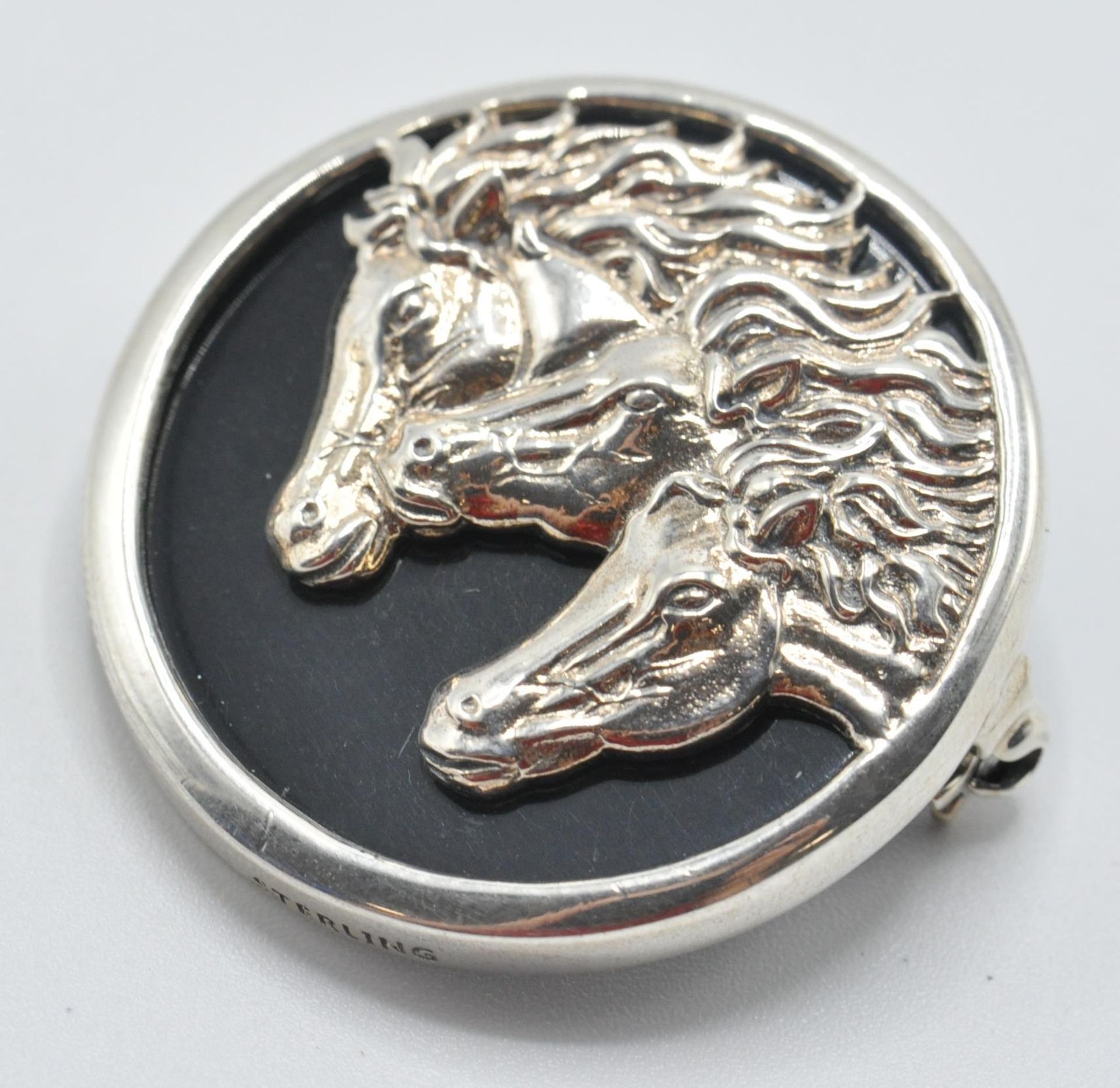 A sterling silver and onyx brooch set with three horse heads. Measures: 3cm diameter. weight 12.8g