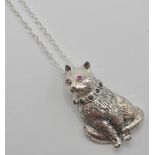 A silver 925 pendant necklace in the form of a sitting cat with red ruby eyes and green sones to the