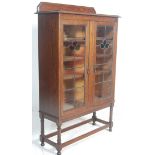 A 1920's oak stained and leaded glass bookcase display cabinet. Raised on block and turned legs