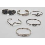A group of silver bangle bracelets to include a buckle design bangle, a wave design bangle, a celtic
