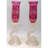 A pair of early 20th Century Baccarat Dauphin Candlesticks having cut glass cranberry hurricane