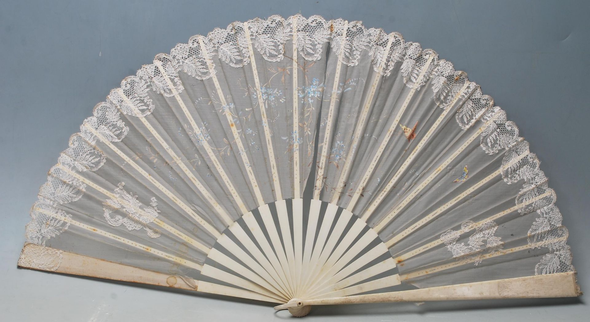 A late 19th / early 20th Century bone and lace hand fan being hand painted with butterflies and