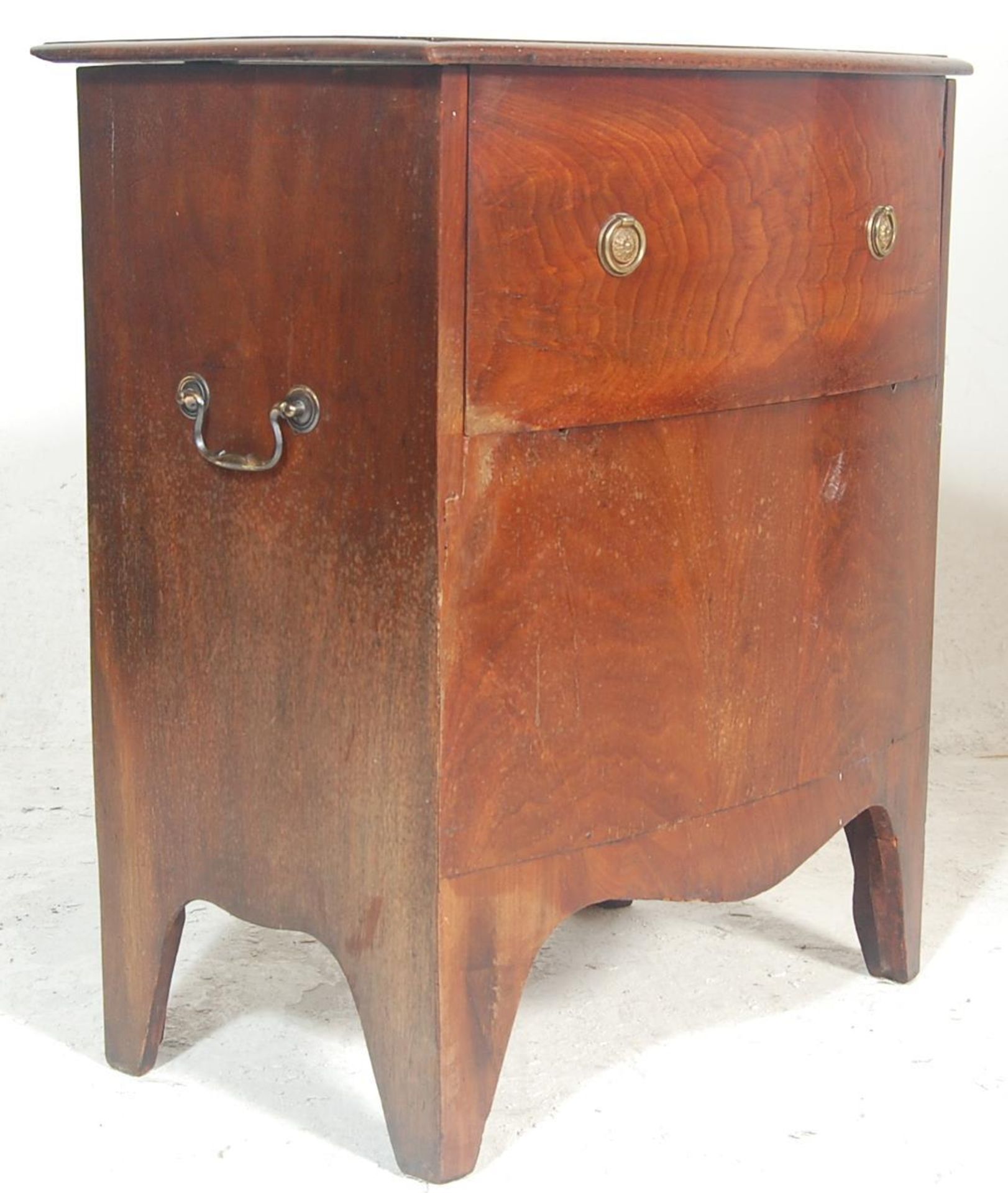 A Regency Revival III bow front commode having circular brass handles under a hinged lid opening