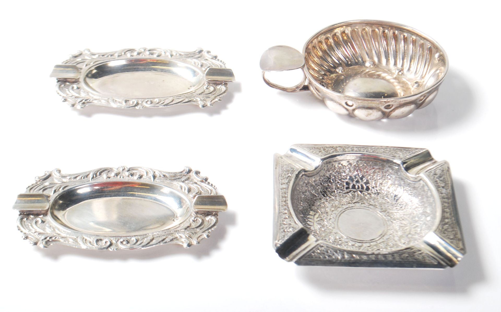 A group of four silver items to include a pair of continental silver ashtrays of oval form having