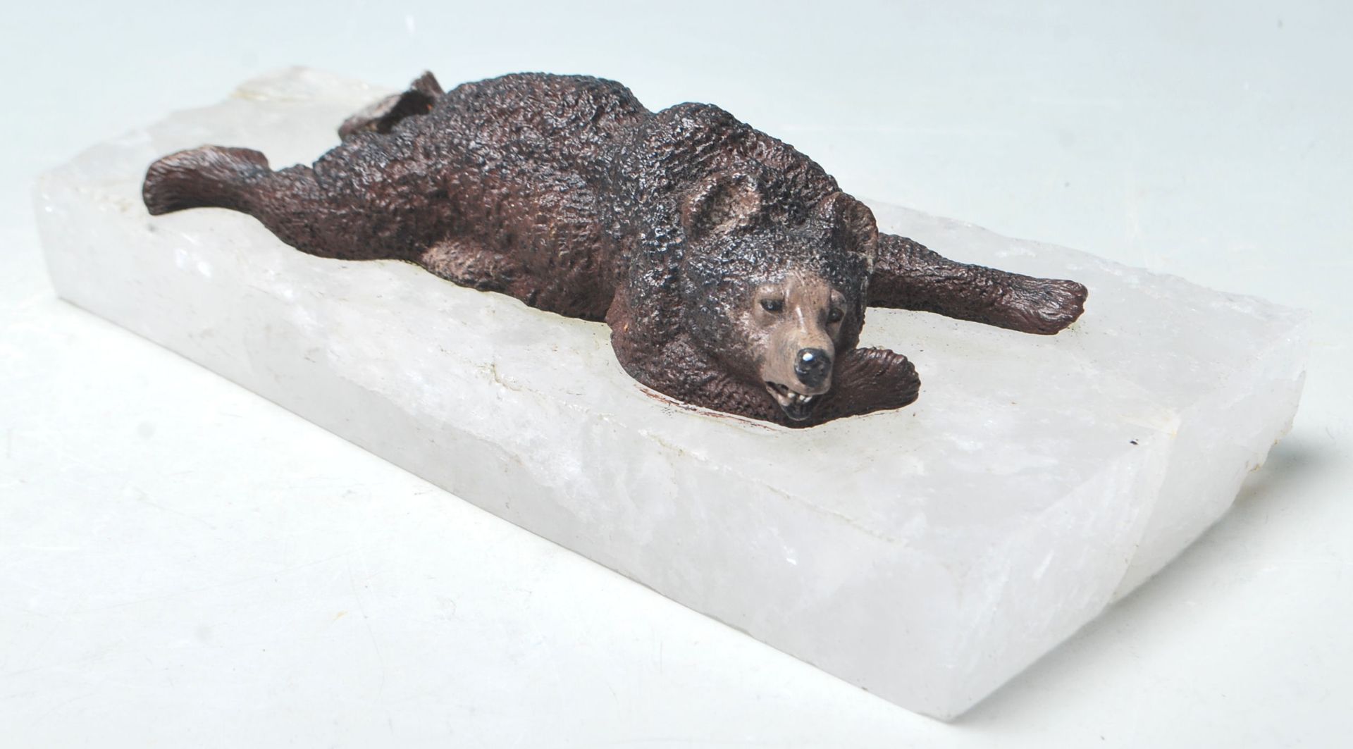 A PAPER WEIGHT COMPRISED OF A CAST IRON BEAR LAYING UPON A QUARTZ BASE