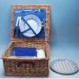 A VINTAGE RETRO WICKER PICNIC BASKET COMPLETE WITH PLATES, KNIVES, FORKS AND THERMOS.