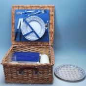 A VINTAGE RETRO WICKER PICNIC BASKET COMPLETE WITH PLATES, KNIVES, FORKS AND THERMOS.