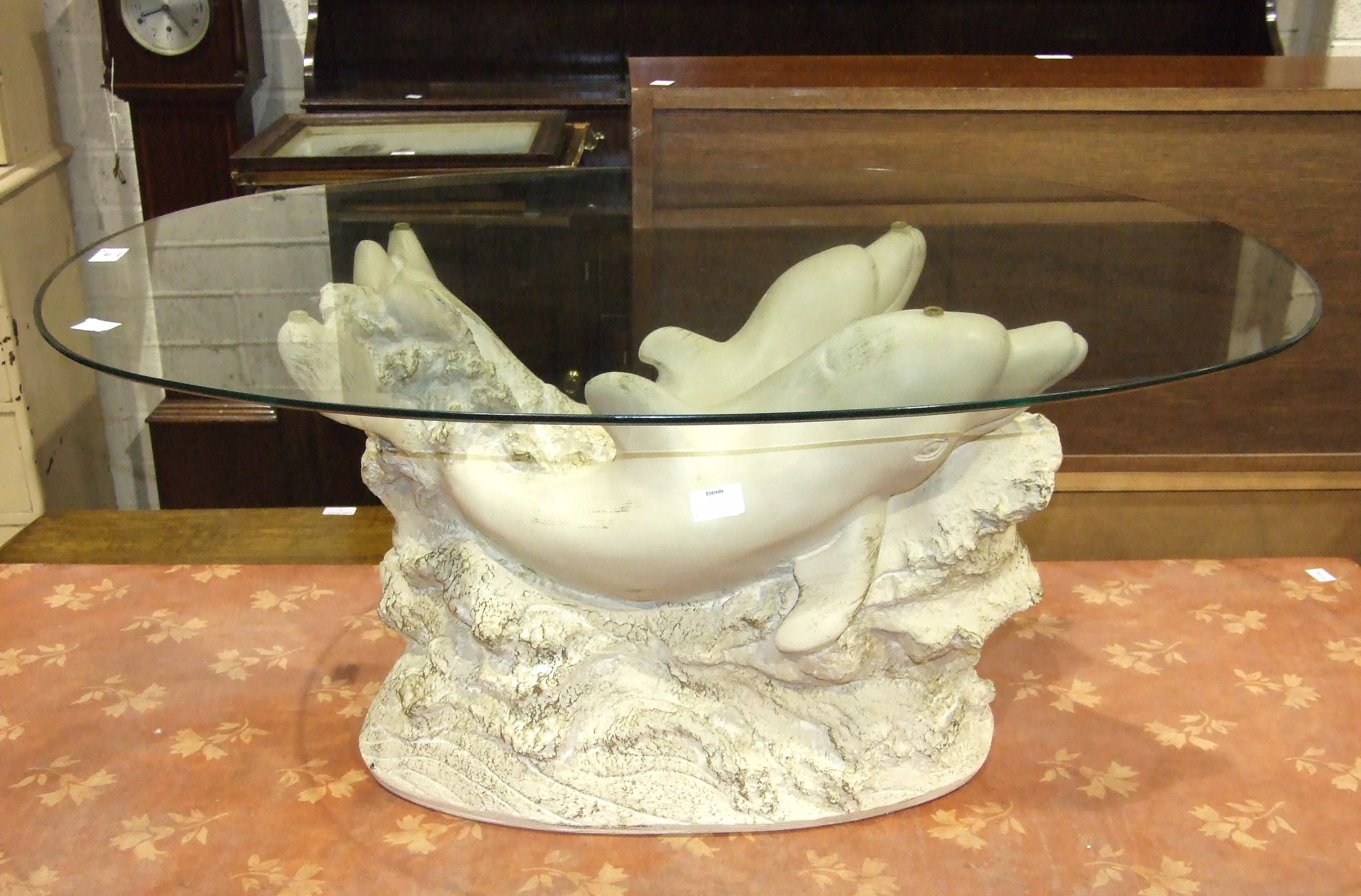 A modern composite coffee table, the base in the form of two dolphins supporting an oval glass