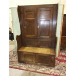 An antique oak bacon settle, the tall back having a pair of panelled doors above the seat with