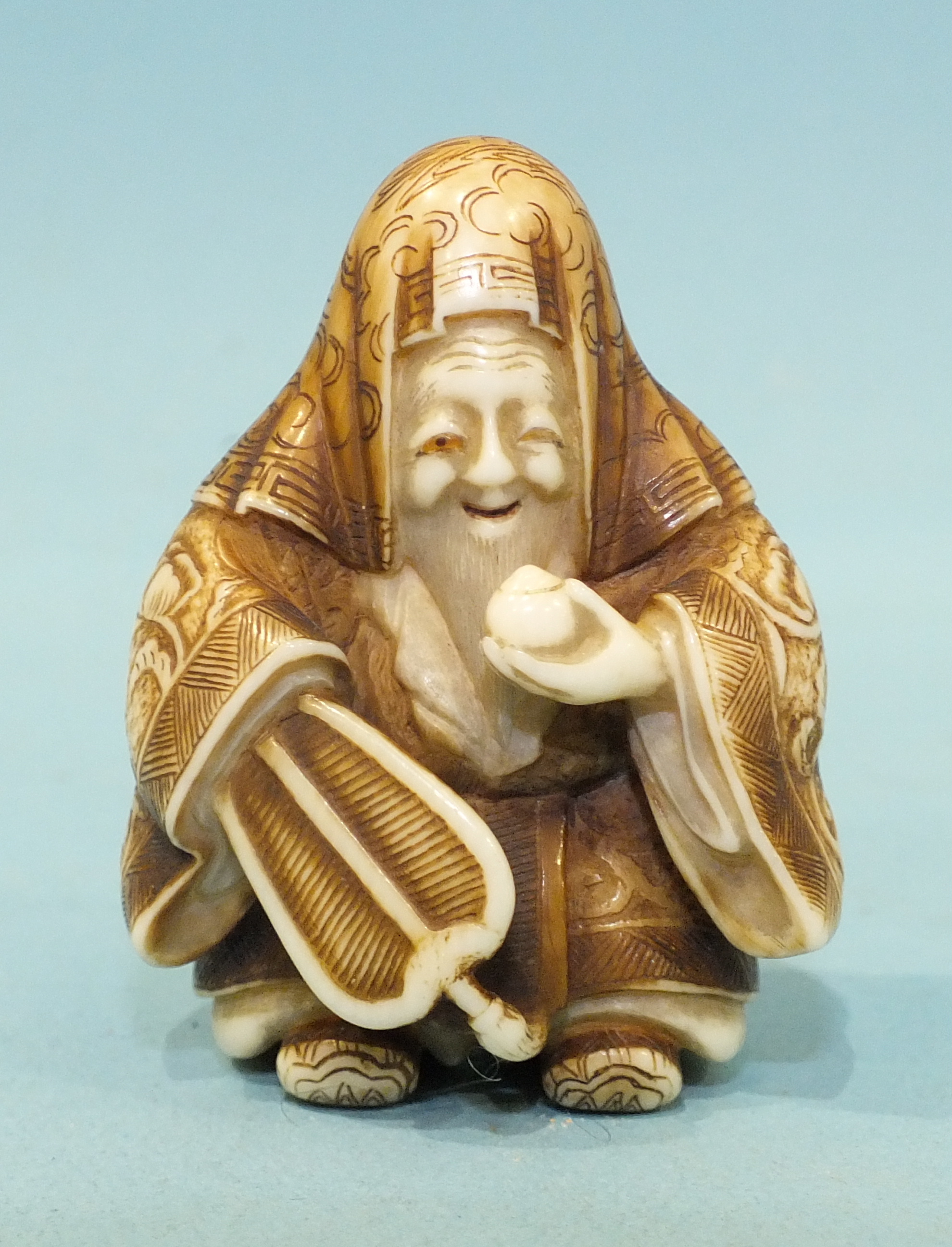 A mid to late-19th century ivory netsuke of Jurojin holding a fan and a tama, his robes finely-