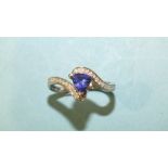 A tanzanite and diamond cross-over ring claw-set a trilliant-cut tanzanite between diamond point-set