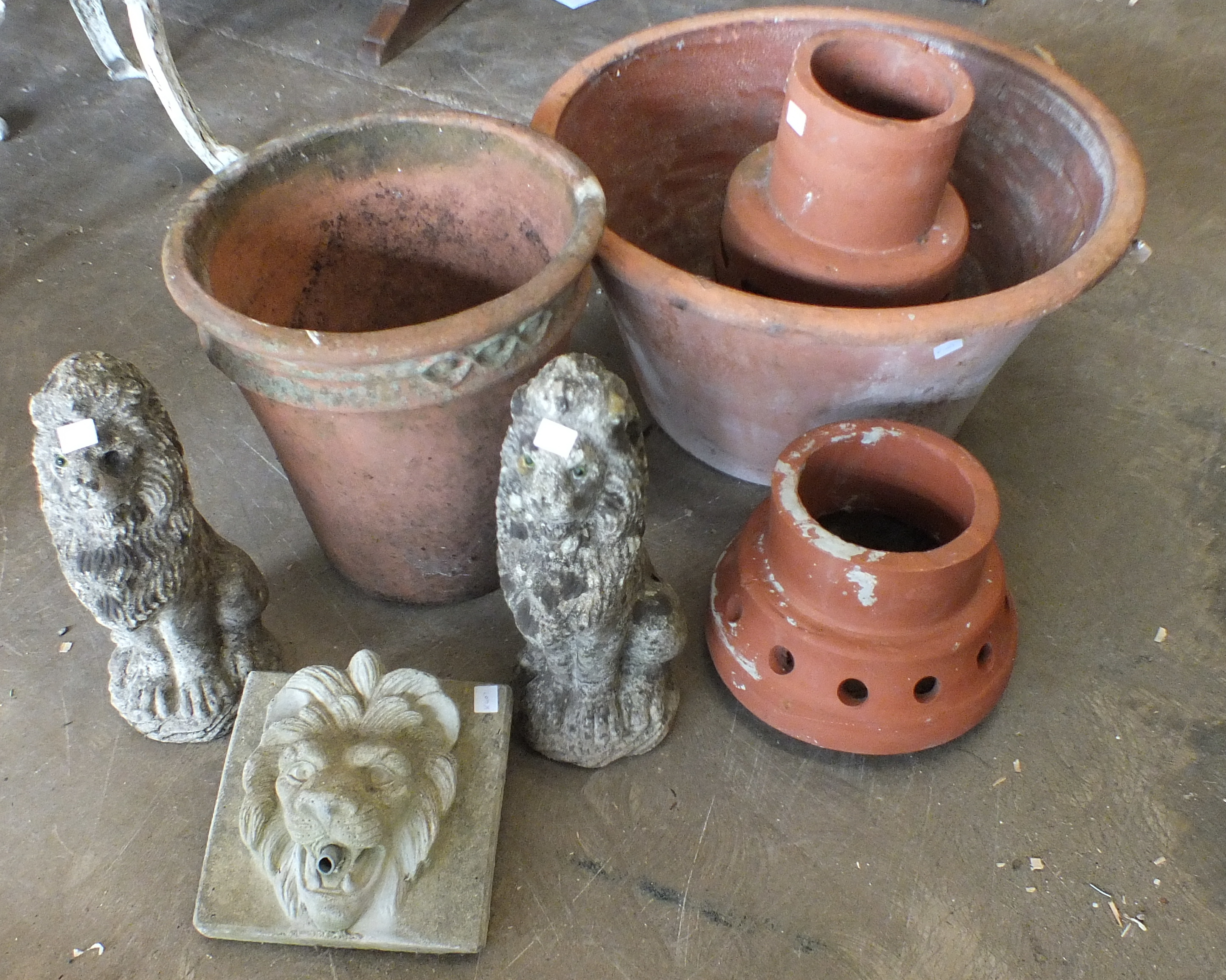 A lion's head fountain, a pair of concrete lion garden ornaments and four terracotta pots.