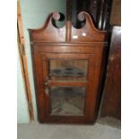 An antique oak hanging corner cupboard with swan-neck pediment above a glazed door, 74cm wide, 115cm