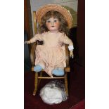 A Continental bisque-headed doll with sleeping eyes, (head cracked), in wood rocking chair.