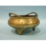 A Chinese bronze metal censer of compressed form, with pierced handles, on three feet, 23cm