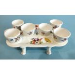 A mid-19th century English porcelain egg cup stand, complete with six matching egg cups, on paw