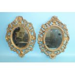 A pair of gilt wood scroll and shell oval frames, each beaded bezel enclosing a later mirrored