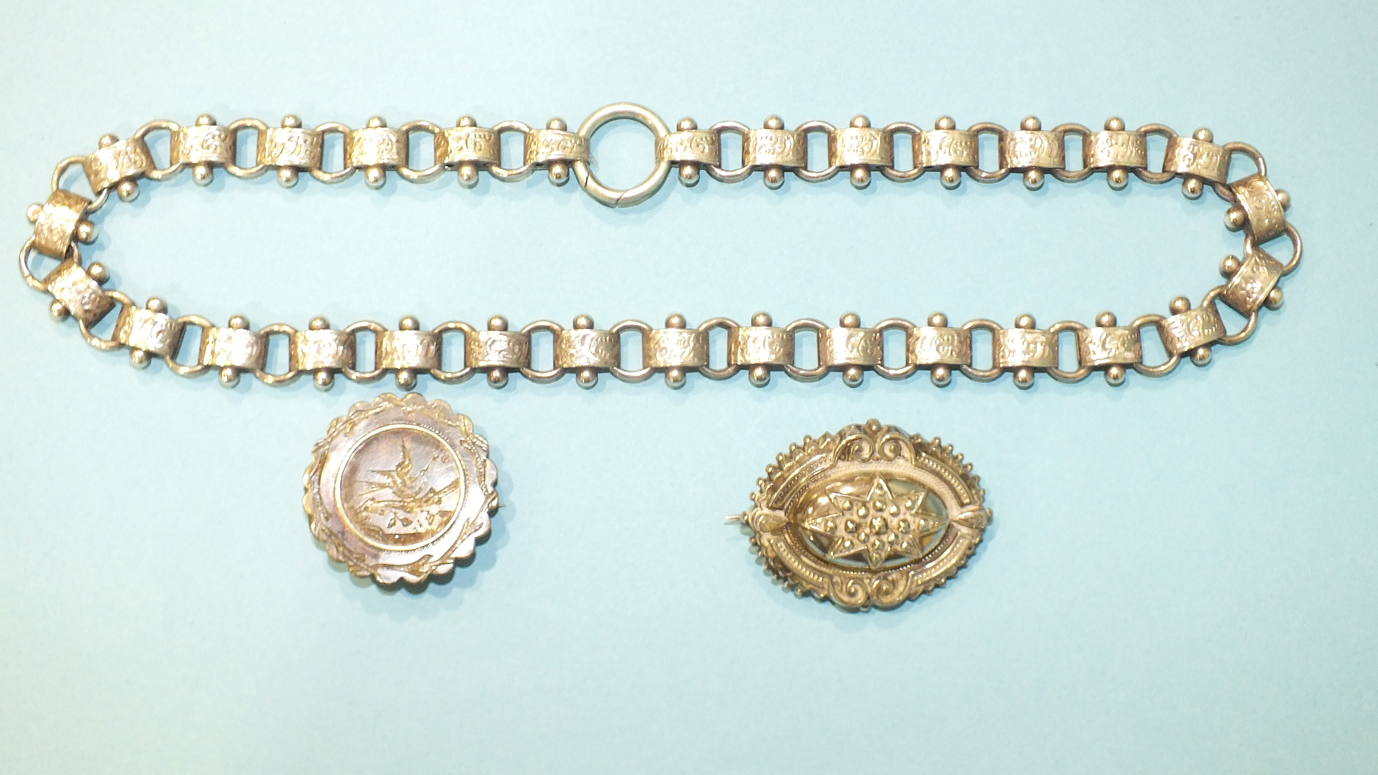 A Victorian silver necklace of engraved links and two silver locket-back brooches, (1 a/f), (3).