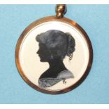 A small Edwardian circular locket pendant containing a silhouette of a young lady, painted in