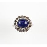 Art Deco period ring set with a central blue cabochon sapphire, within a border of white