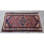 Persian red ground rug with central navy blue medallion, stylised floral decoration, multiple