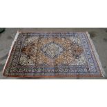 Persian silk burnt-orange ground carpet, with a main blue border, centre of which has concentric