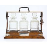 Edwardian oak and silver plated tantulus with three decanters with presentation plate. 38cm length..