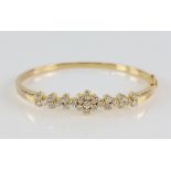 Gold oval hinged bangle, set with round brilliant cut diamonds, with a central floral cluster,
