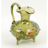 Green glass water jug on three feet, painted in enamels with Persian flower decoration and prunts,