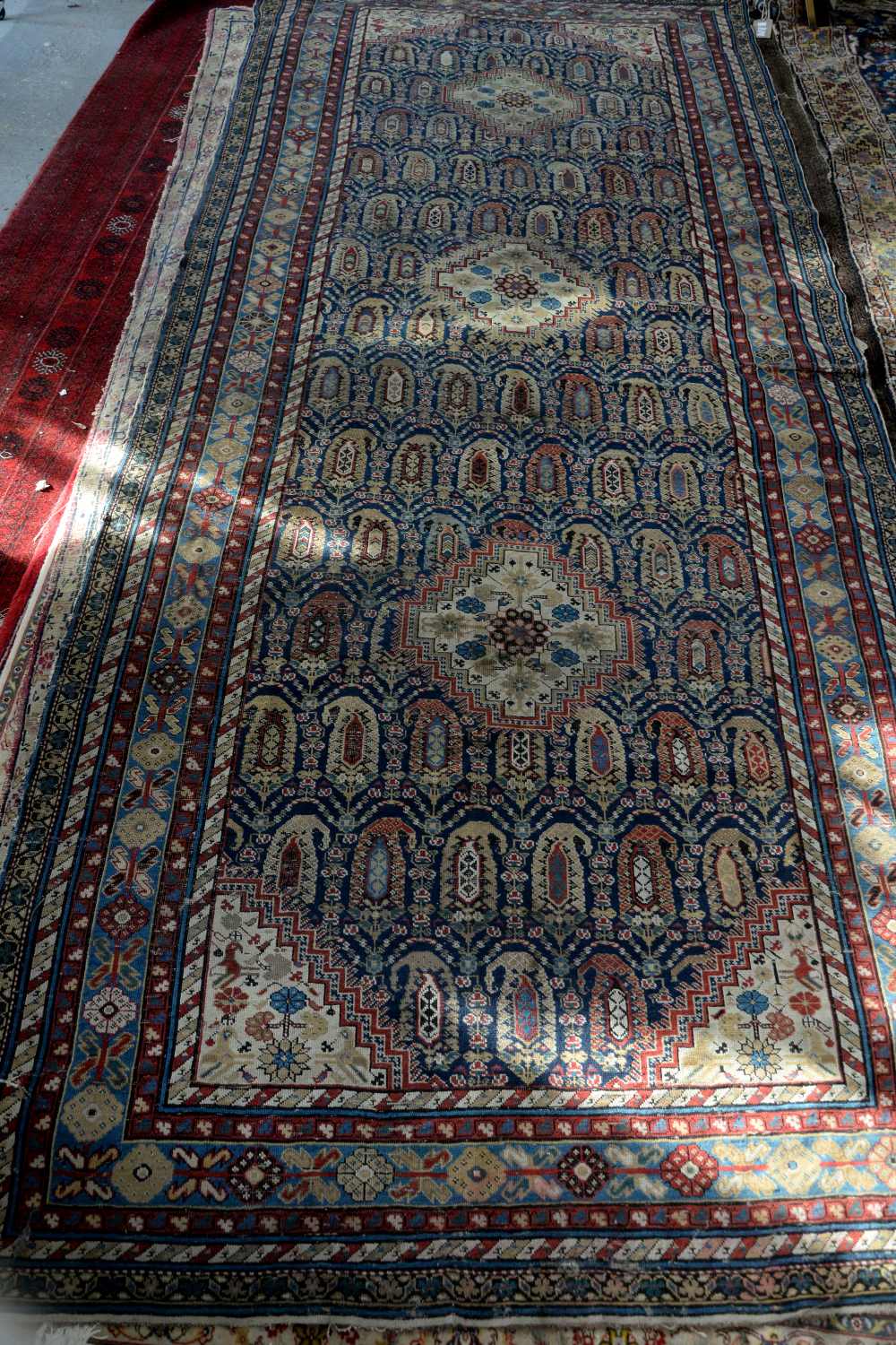 Tribal carpet with repeating Boteh motifs and three geometric medallions on a blue ground, within
