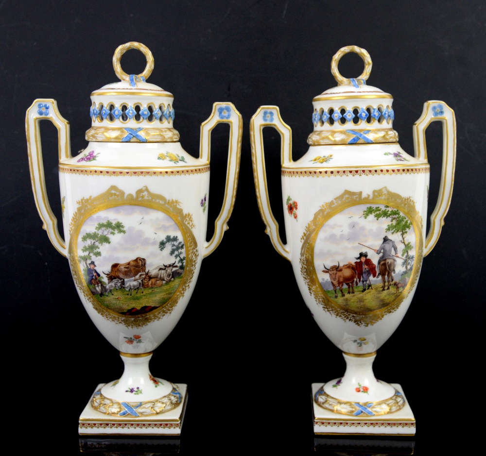 A pair of two handled Continental porcelain urns and covers with central cartouches painted with