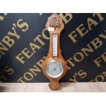 AN ANEROID BAROMETER IN CARVED OAK CASE