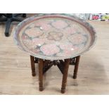 A MIDDLE EASTERN BRASS CIRCULAR TRAY ON CARVED WOODEN STAND 62CM DIAMETER