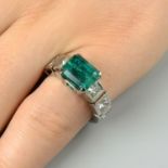 An emerald single-stone ring, with square-shape diamond panel shoulders.