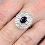 A mid 20th century platinum and gold sapphire and brilliant-cut diamond cluster ring.Sapphire