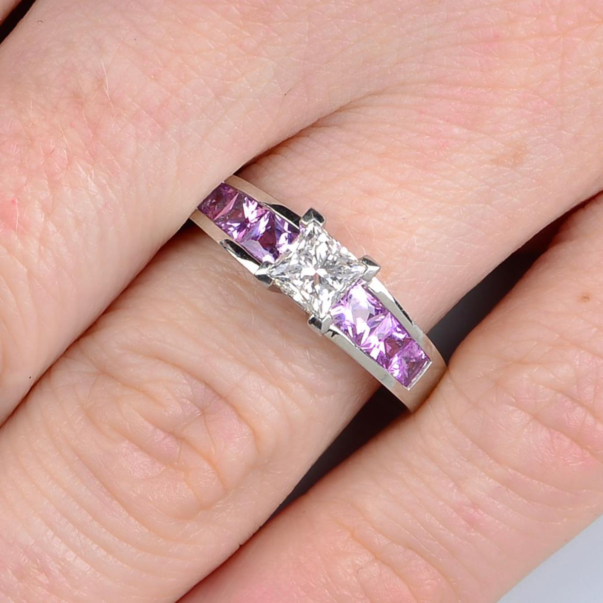 A platinum diamond single-stone ring, with square-shape pink sapphire line gallery and shoulders.