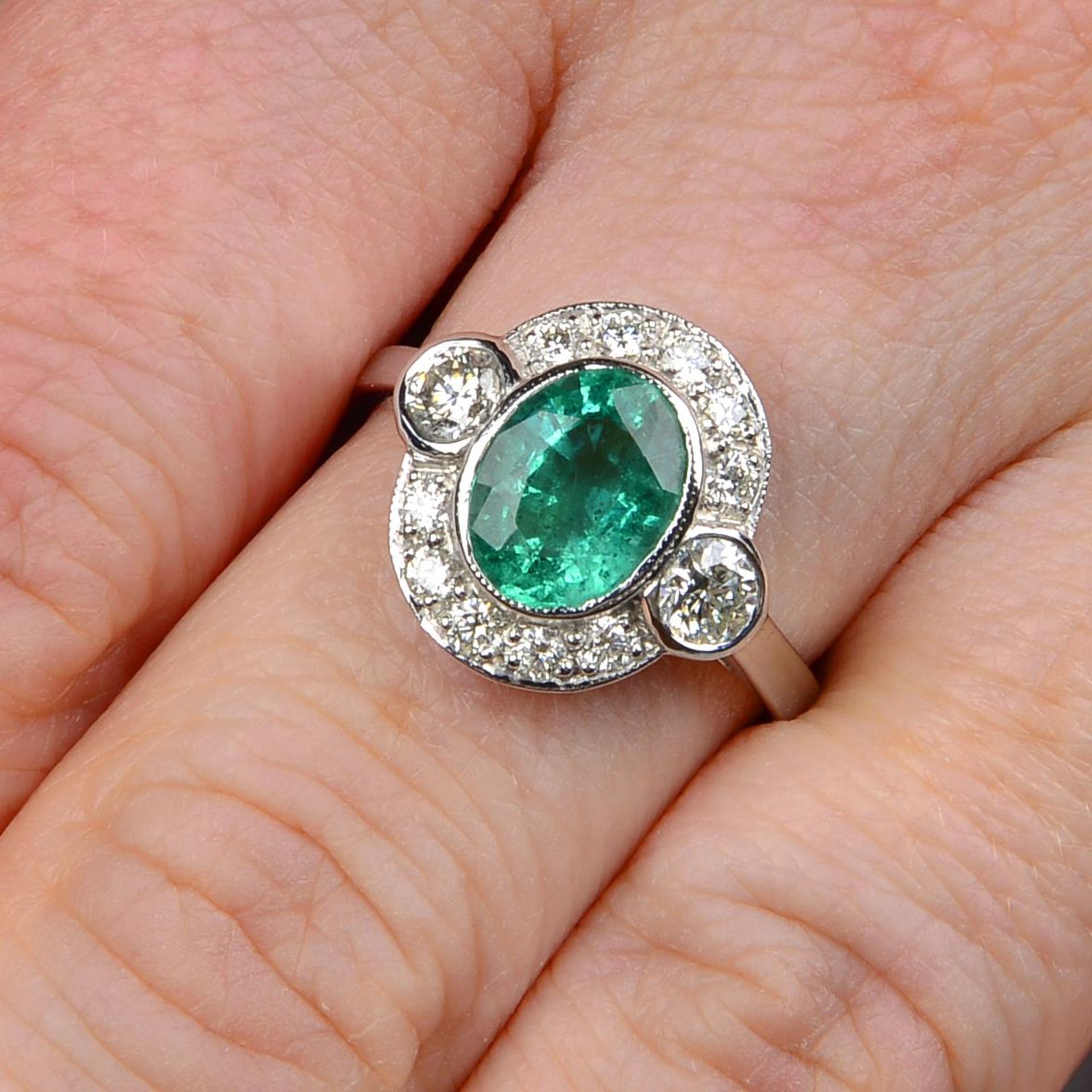 An emerald and brilliant-cut diamond cluster ring.Emerald calculated weight 1.48cts,