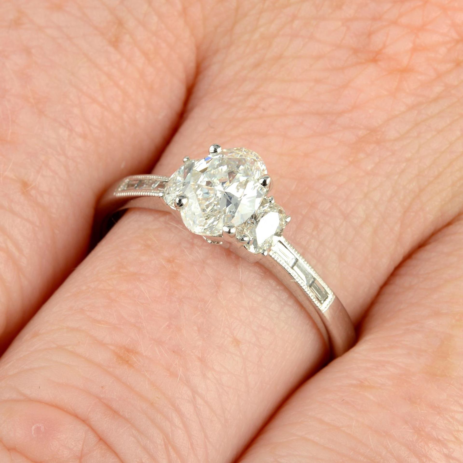 An oval-shape diamond single-stone ring, with oval-shape and baguette-cut diamond sides.