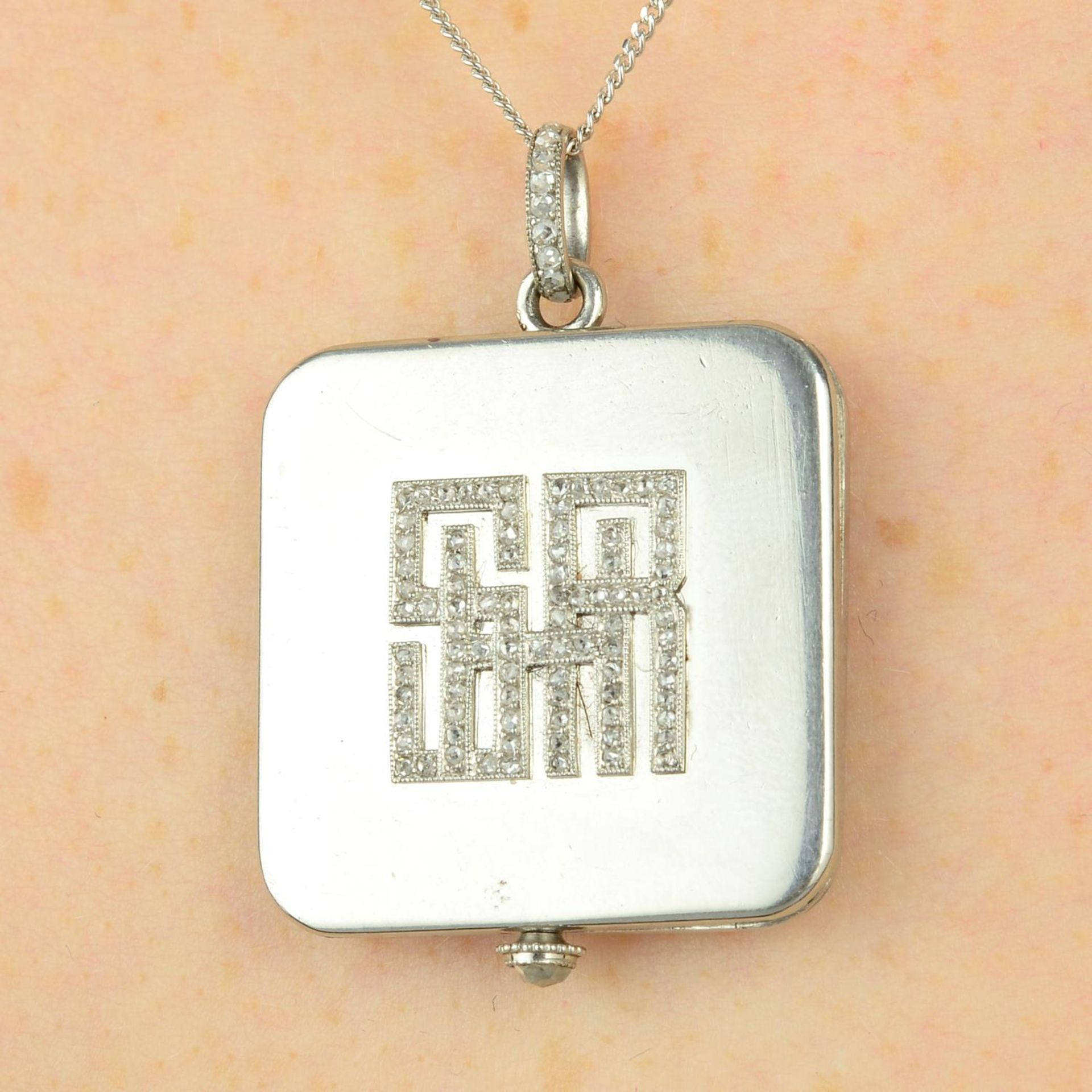 An Art Deco platinum pendant watch, with rose-cut diamond monogram and highlights, by Cartier.