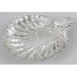 A late Victorian silver dish in the form of a scallop shell and raised on three reeded ball feet,