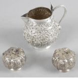 Four assorted items in white metal to include a cream jug, a salt and pepper and a pair of tongs.