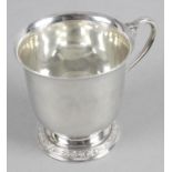 A late 20th century silver Christening mug of plain form standing on a footed base with decorative