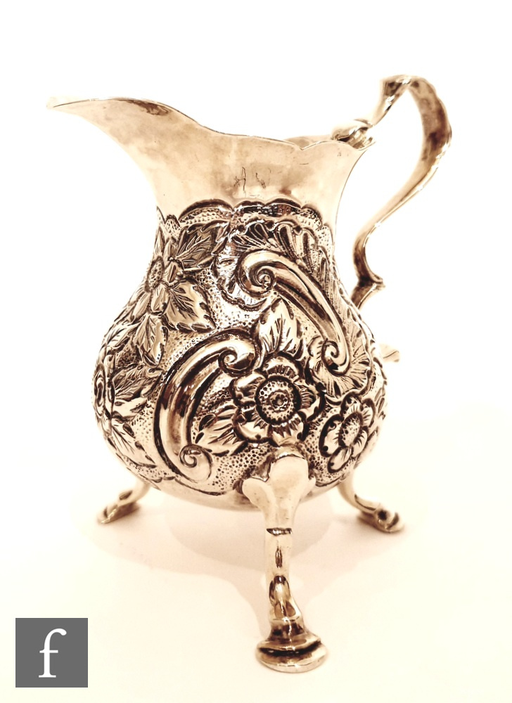 A Georgian hallmarked silver cream jug with later part foliate engraved decoration raised on three