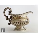A George III hallmarked silver melon shaped pedestal cream jug terminating in acanthus capped scroll