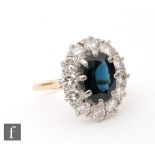 An 18ct sapphire and diamond cluster ring, central oval sapphire within a border of twelve brilliant