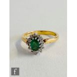 An 18ct hallmarked emerald and diamond cluster ring, central oval emerald within a diamond surround,