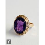 A 14ct single stone amethyst ring, claw set oval stone to a pierced border and plain shoulders,